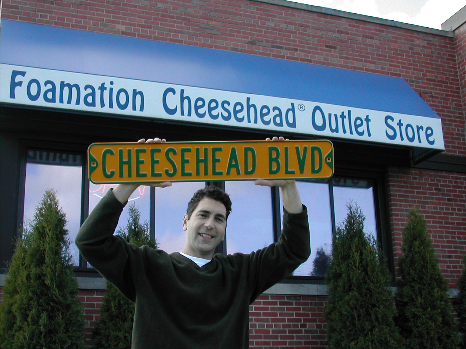 Ralph Bruno, the Cheesehead creator, stands outside the Foamation Inc. Cheesehead Outlet Store.  Foamation sells a variety of spin-offs, including the Cheesehead Ave. road sign. Photo by Michelle Wexler