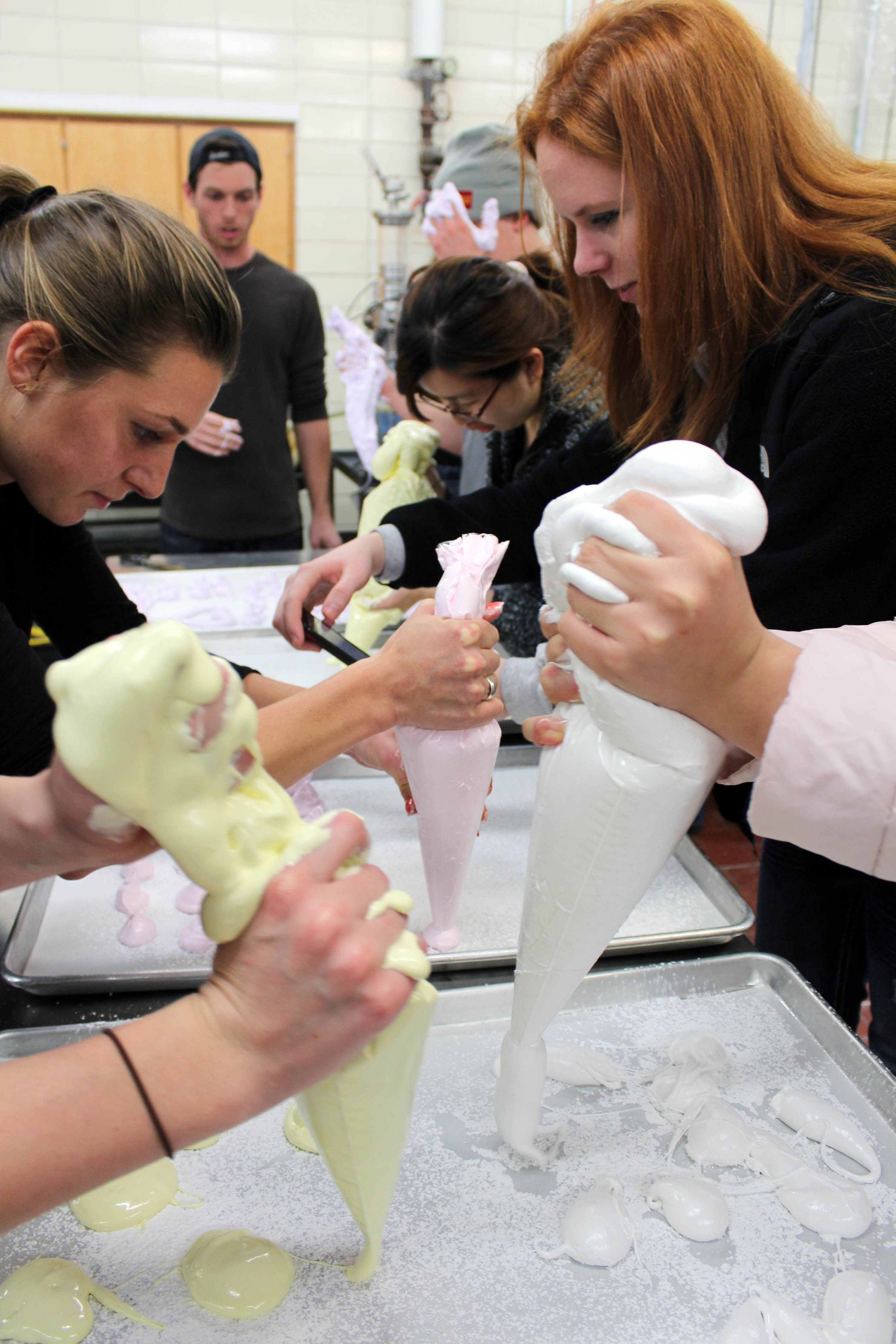 Students use icing bags to pipe their marshmallow fluff onto starch trays in the last step of the marshmallow making process.