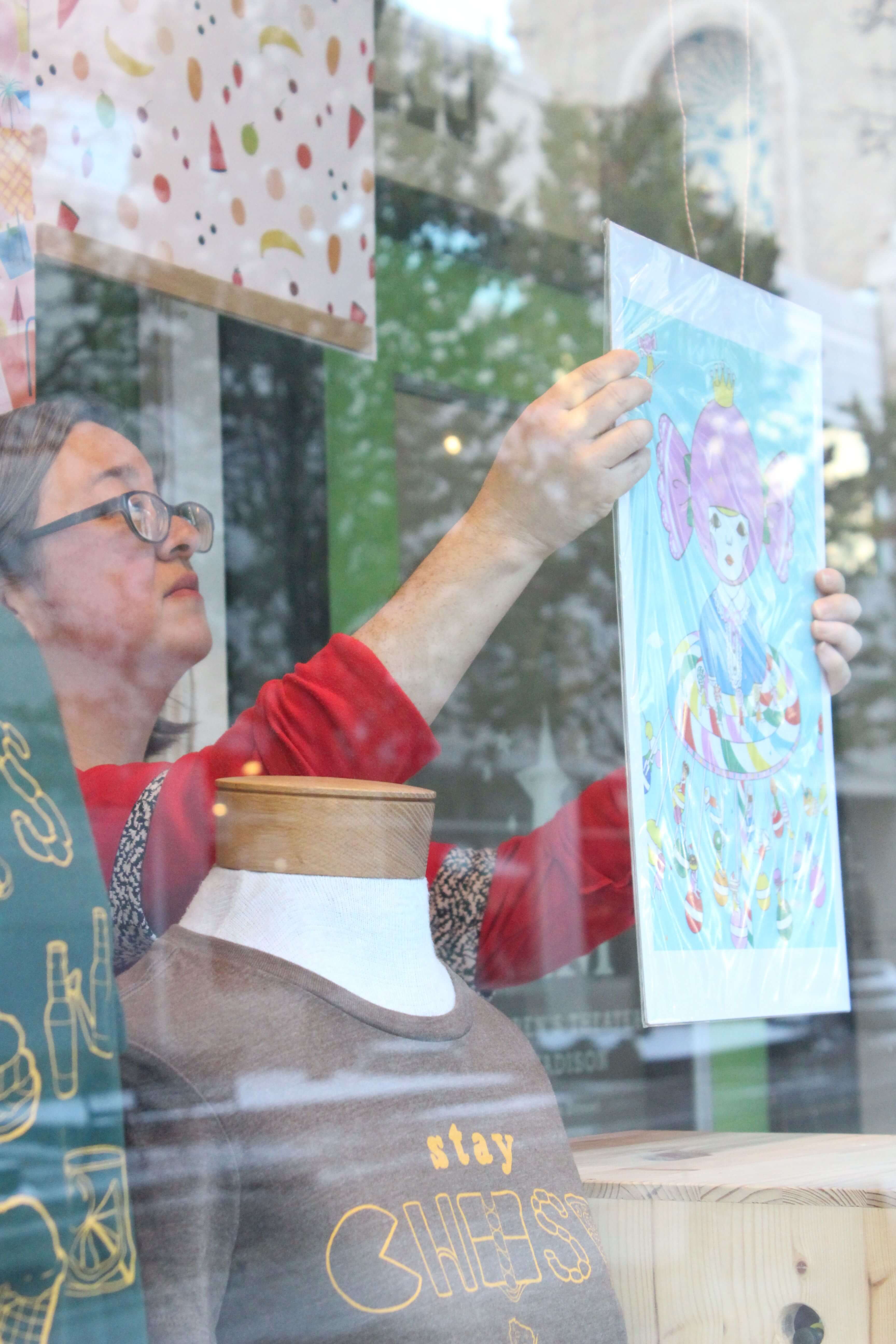 Laura Komai hangs artwork for display in Anthology's window.