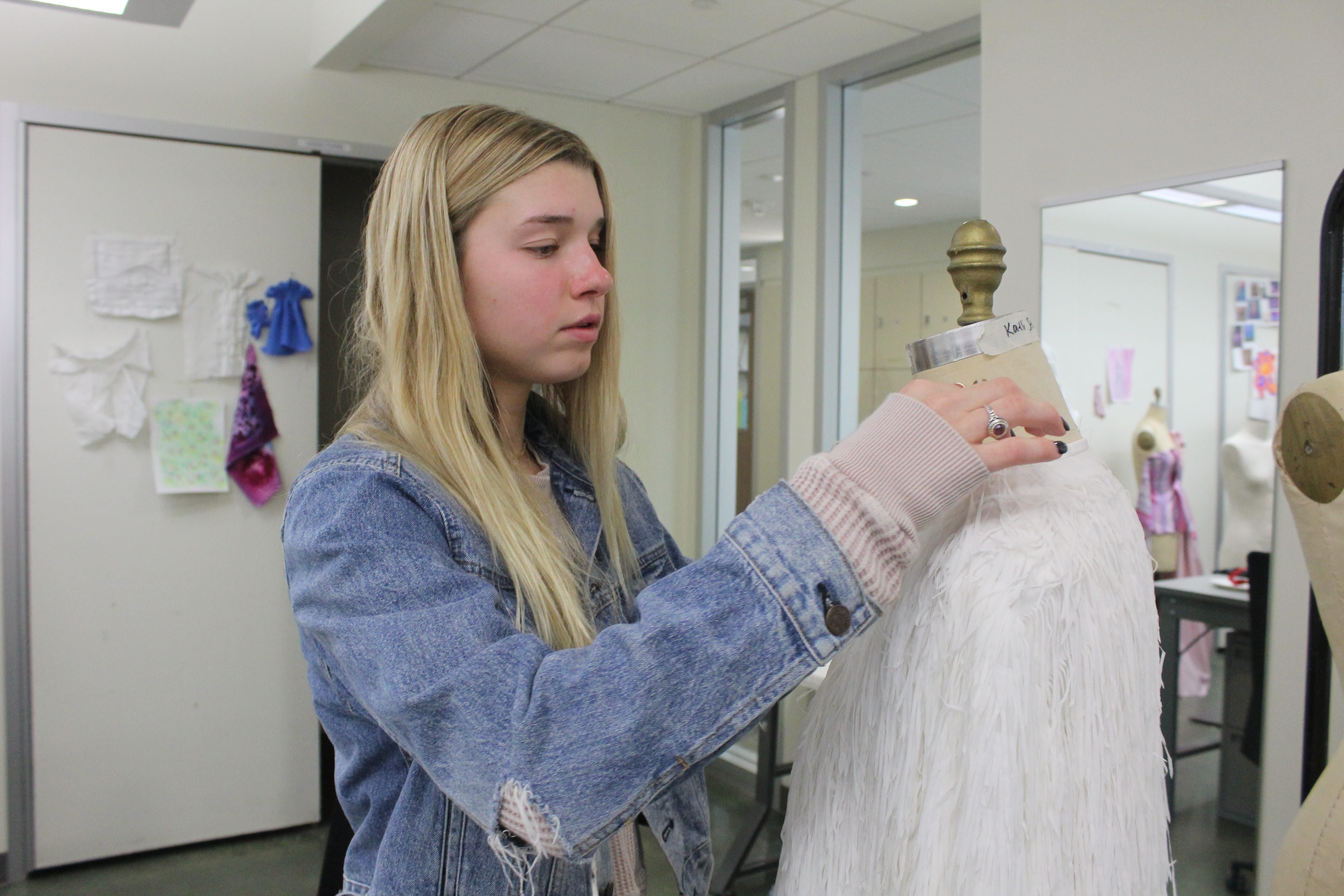 Erin Schaut, a fashion student at UW-Madison, pins up a white jacket she created onto a mannequin.