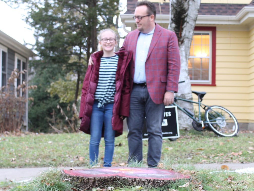 Mike Wagner and daughter, Eleanor, stand behind the stump of an ash tree on Nov. 19, 2019. The city-owned ash tree was removed from in front of their home in Madison, Wisconsin. Photo by Kathryn Wisniewski